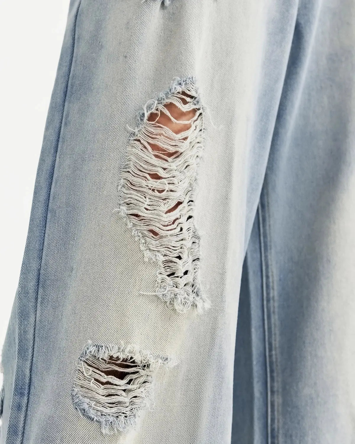 Distressed ripped blue jeans by INFLATION featuring a trendy streetwear style with frayed holes and faded denim.