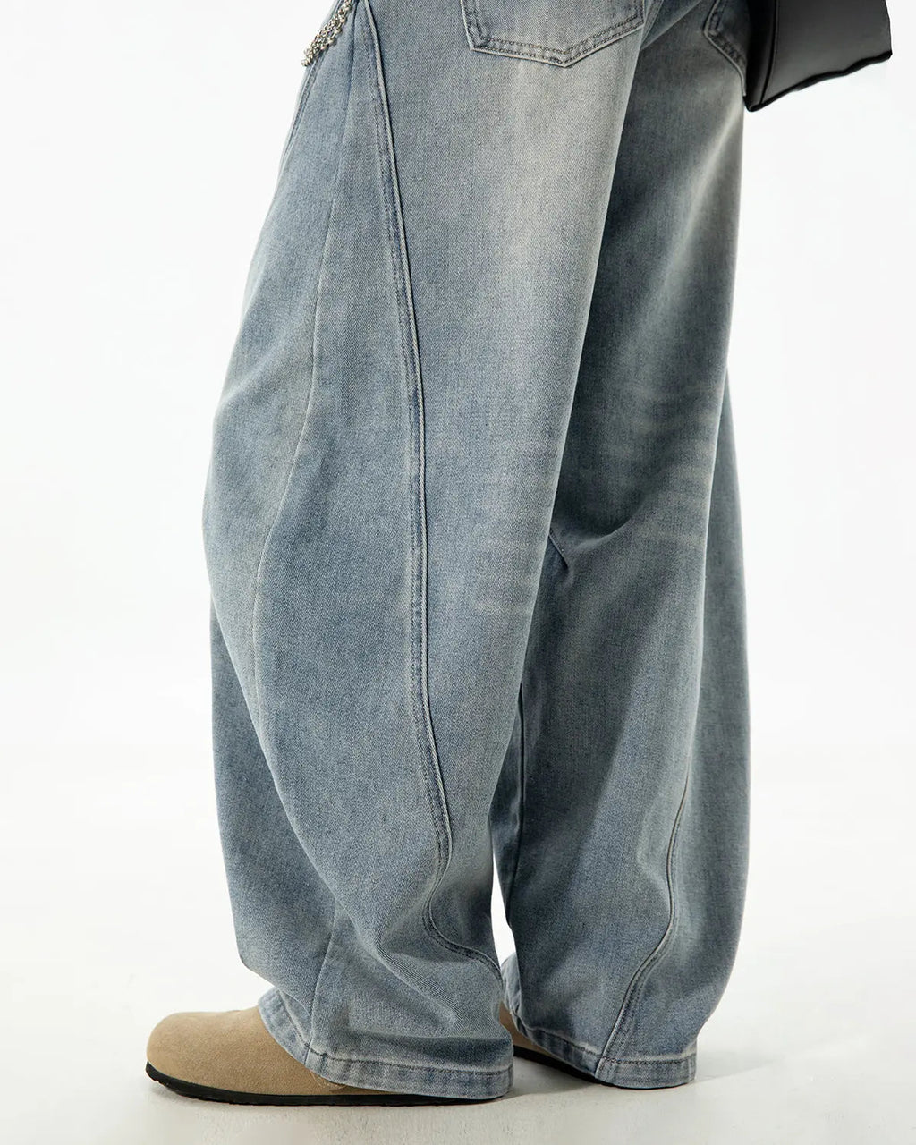 Curved seam deconstructed barrel jeans by Inflation Streetwear with distressed detailing and relaxed fit, shown on a hanger.
