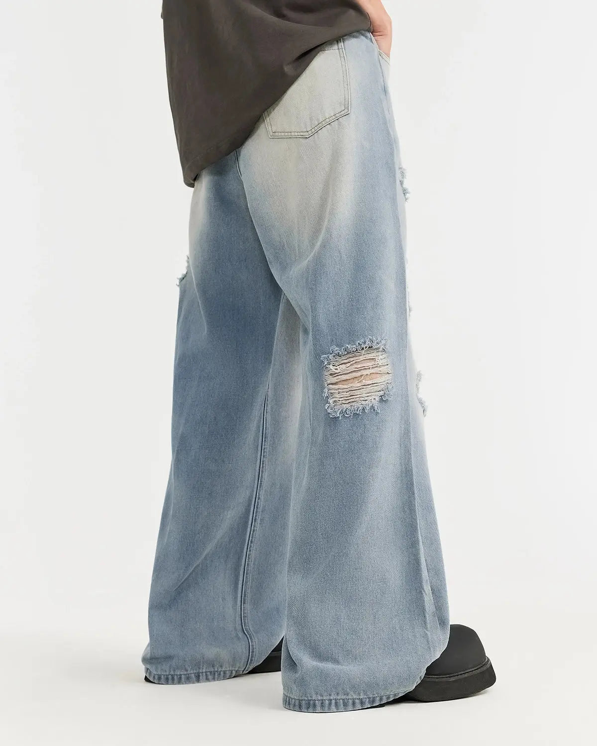 Distressed ripped blue jeans from Inflation Streetwear with frayed holes and a casual fit, showcasing trendy denim style.