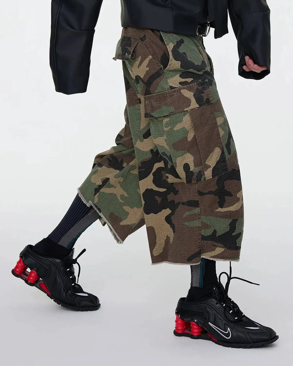 Inflation Streetwear oversized camo cargo longline shorts with large pockets and relaxed fit, featuring green and brown camouflage pattern.