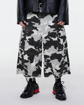 Glitter camo cargo longline shorts by INFLATION, featuring shiny fabric, multiple pockets, and a relaxed streetwear style.