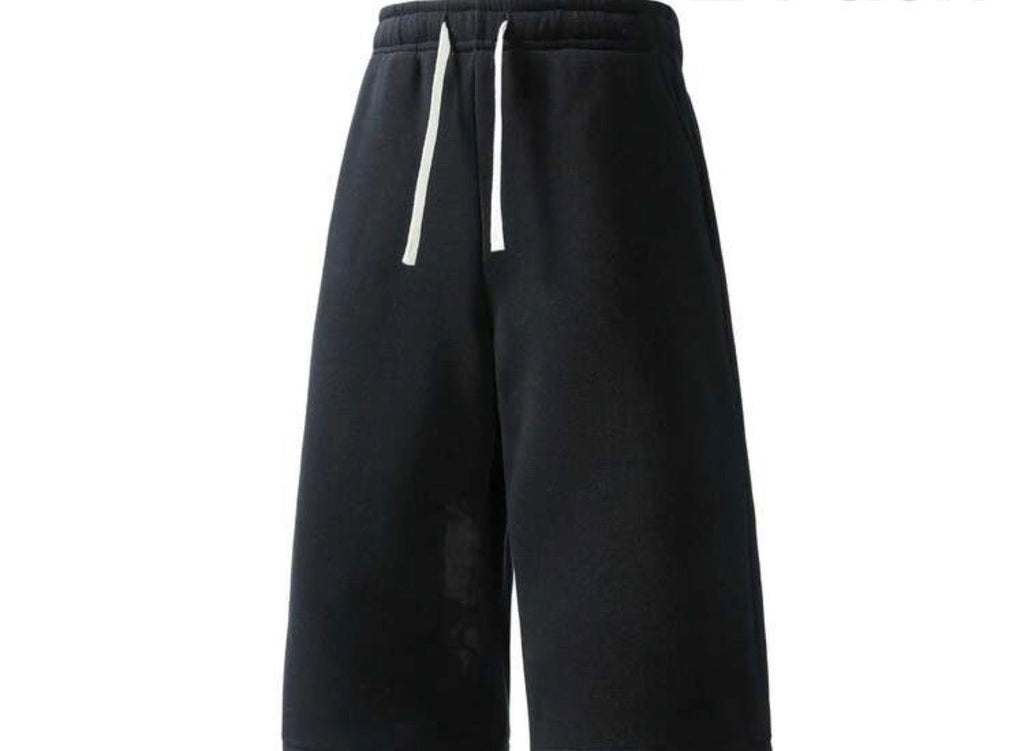 Inflation trending long jogger shorts in black, featuring a relaxed fit, elastic waistband, and side pockets on a model.